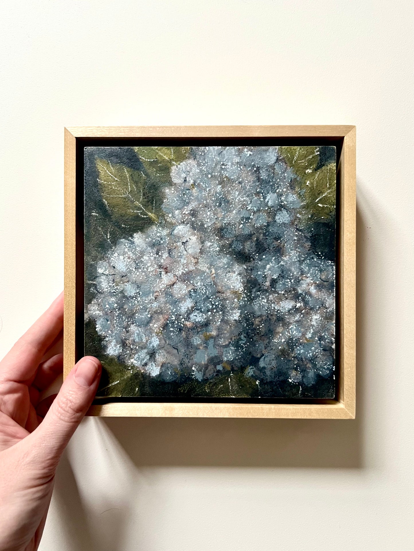 Framed artwork of a floral design held by a hand on a light background