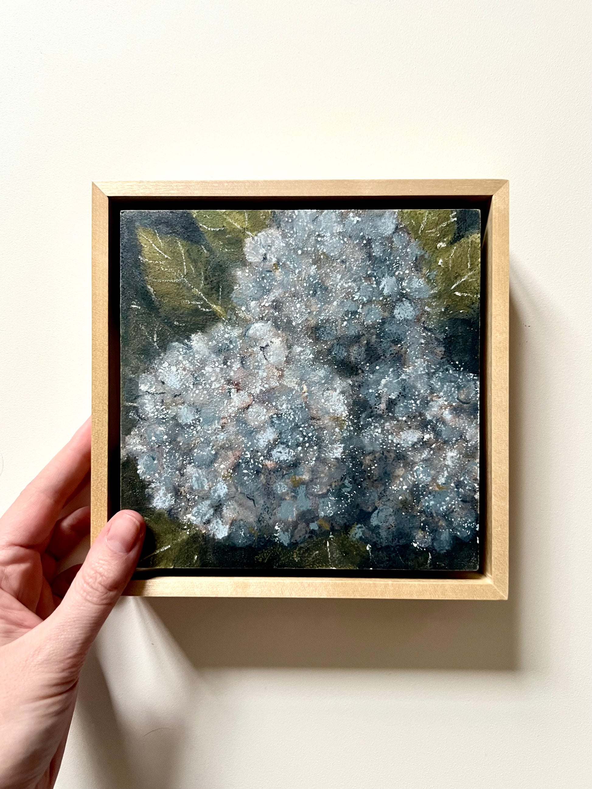 Framed artwork of a floral design held by a hand on a light background