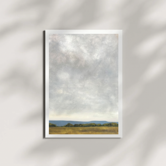 artwork of a landscape with a field and trees under a cloudy sky on a white wall.